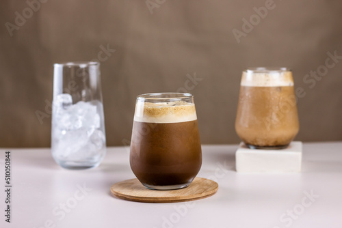 Cold coffee summer drink concept. Different size transparent glasses with ice cube and iced coffee on pastel brown background. photo