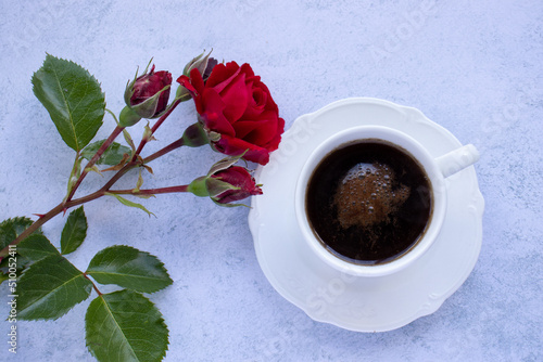 Cup of coffee and red rose flower on table. Top view of espresso black coffee in white porcelain cup on concrete background