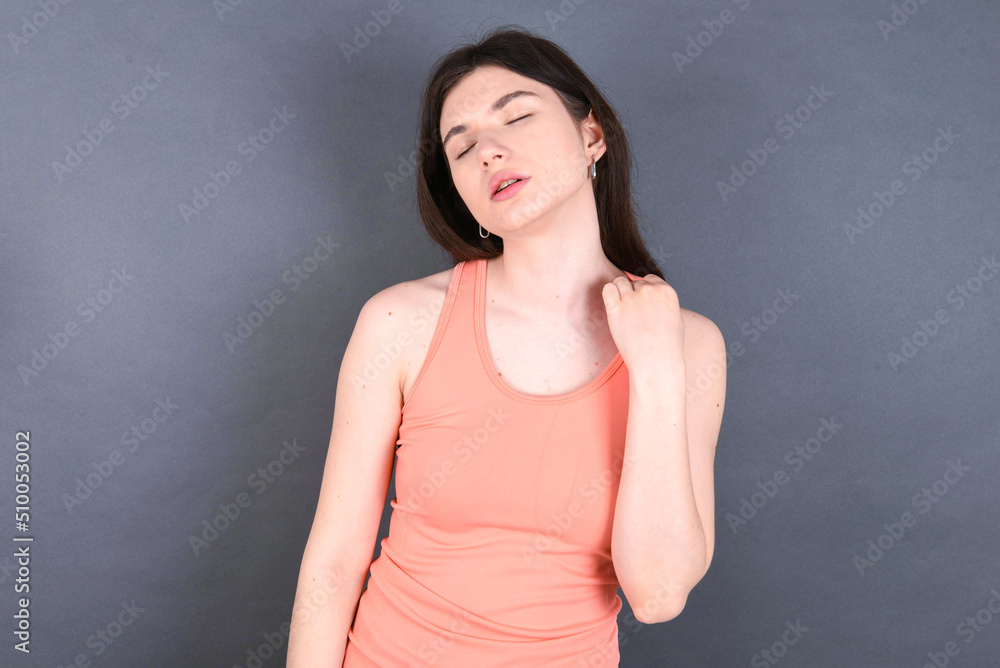 Caucasian woman wearing orange T-shirt over grey wall stressed, anxious, tired and frustrated, pulling shirt neck, looking frustrated with problem Caucasian woman wearing orange T-shirt over grey wall stressed, anxious, tired and frustrated, pulling shirt neck, looking frustrated with problem