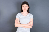 Confident young beautiful Caucasian woman wearing white T-shirt over grey wall with arms crossed looking to the camera