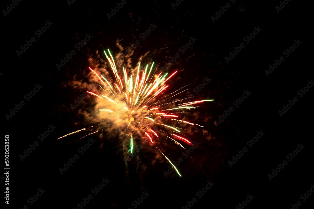 A portrait of fireworks exploding giving us a view on green, red and orange sprakles in the night sky.