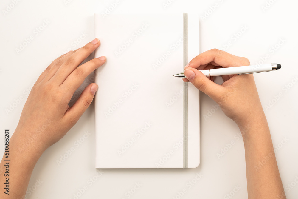 Female hands holding white book with blank cover and white pen on grey background, top view Female hands holding white book with blank cover and white pen on grey background, top view