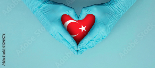 Doctors hands wearing blue surgical gloves making hear shape symbol with turkey flag photo