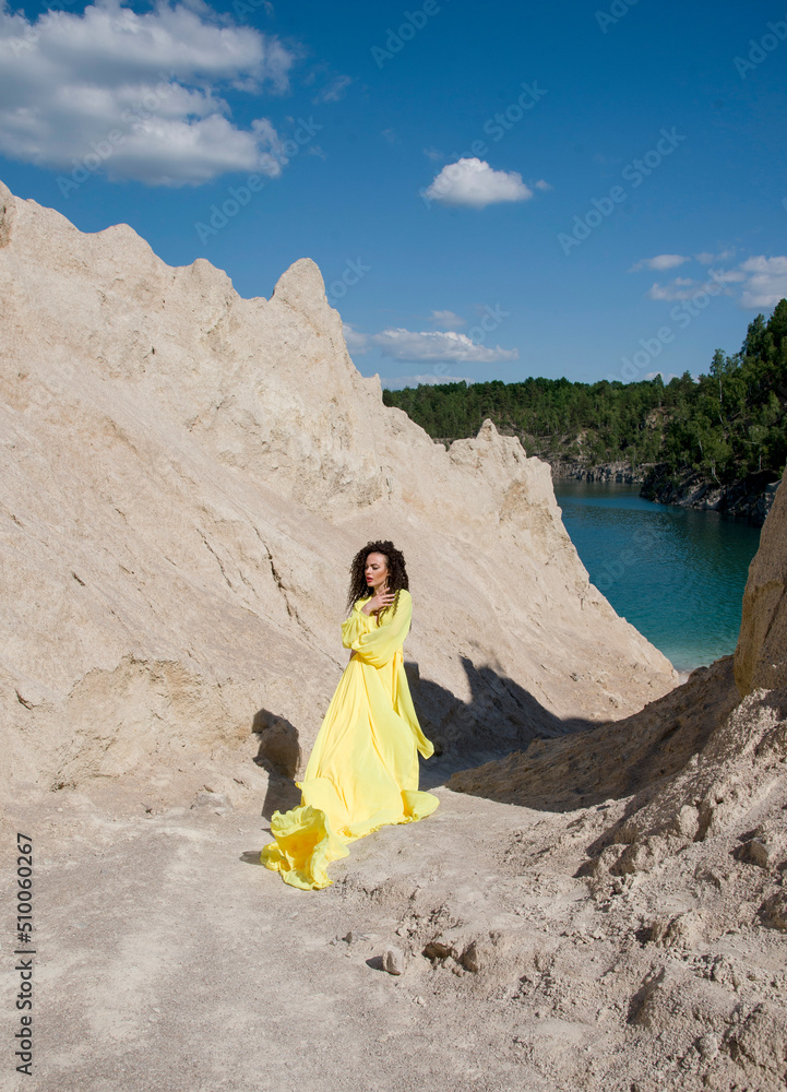 beautiful brunette woman with curly hair walking in long yellow dress on the beach in mountains