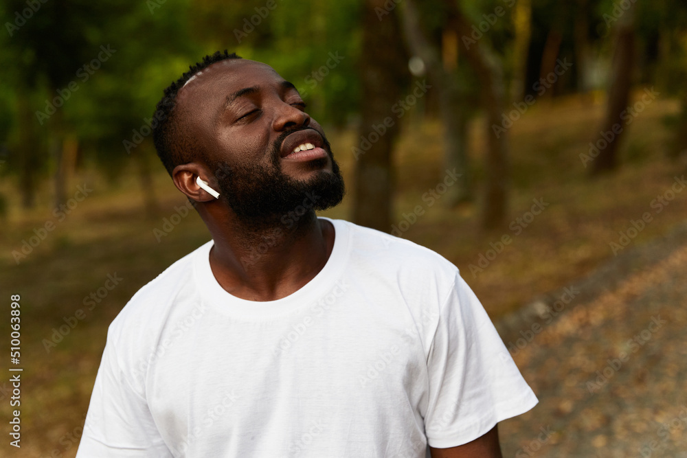 Happy young adult african american man walking in the park wearing headphones Happy young adult african american man walking in the park wearing headphones