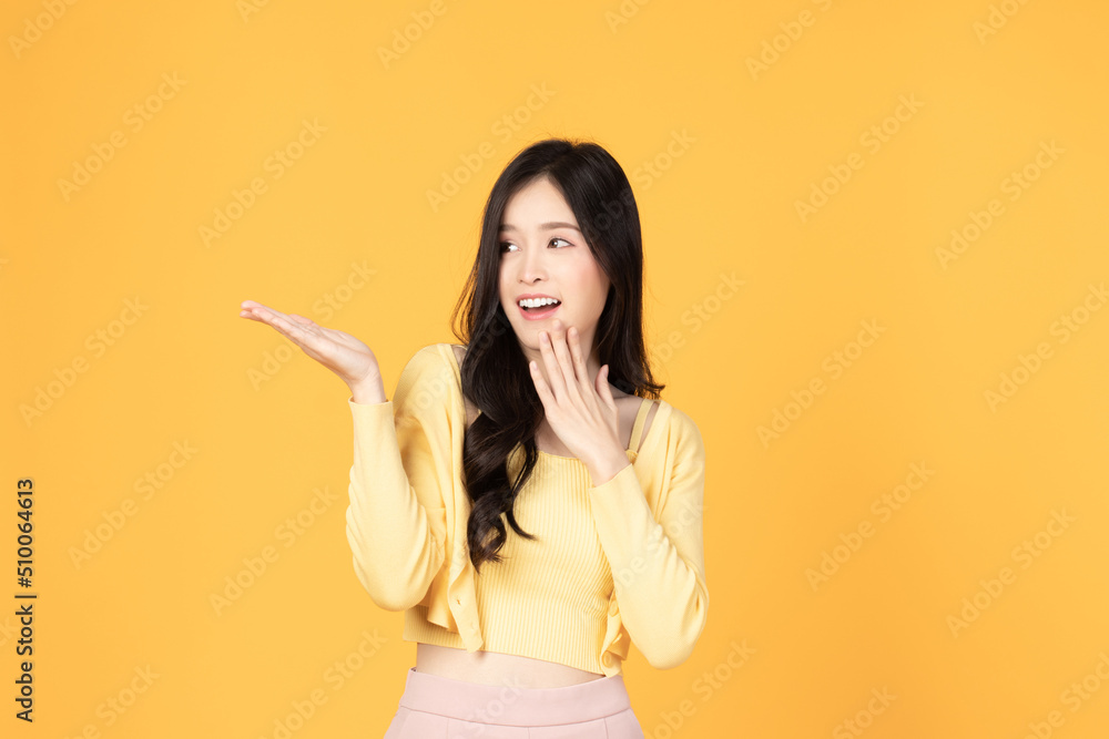 Beautiful Asian woman wearing casual clothes smile and pointing finger to an empty palm isolated on yellow background studio portrait. Beautiful Asian woman wearing casual clothes smile and pointing finger to an empty palm isolated on yellow background studio portrait.