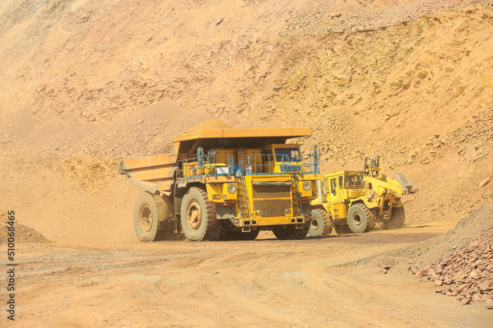 A quarry dump truck loaded with orange rock. Moving large dump trucks around the quarry. Open-pit mining technology. A quarry dump truck loaded with orange rock. Moving large dump trucks around the quarry. Open-pit mining technology.