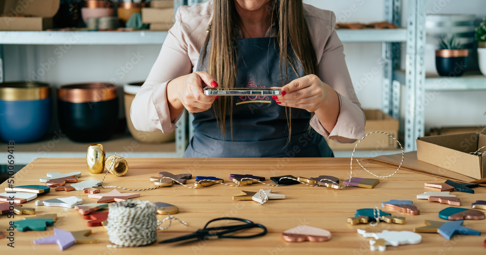 Obraz premium Close Up Photo Of Woman Hands Holding Mobile Phone And Photographing Christmas Ornaments Of Clay At Workshop Desk