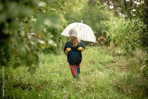 little girl with umbrella in the garden walking away