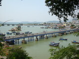 View of a road bridge over a river in a tropical country. Cars and motorbikes are driving along the bridge. Boats are in the river.
