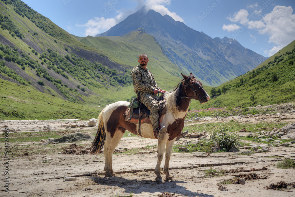 Naklejka premium A man is sitting on a horse. In the background are high mountains.