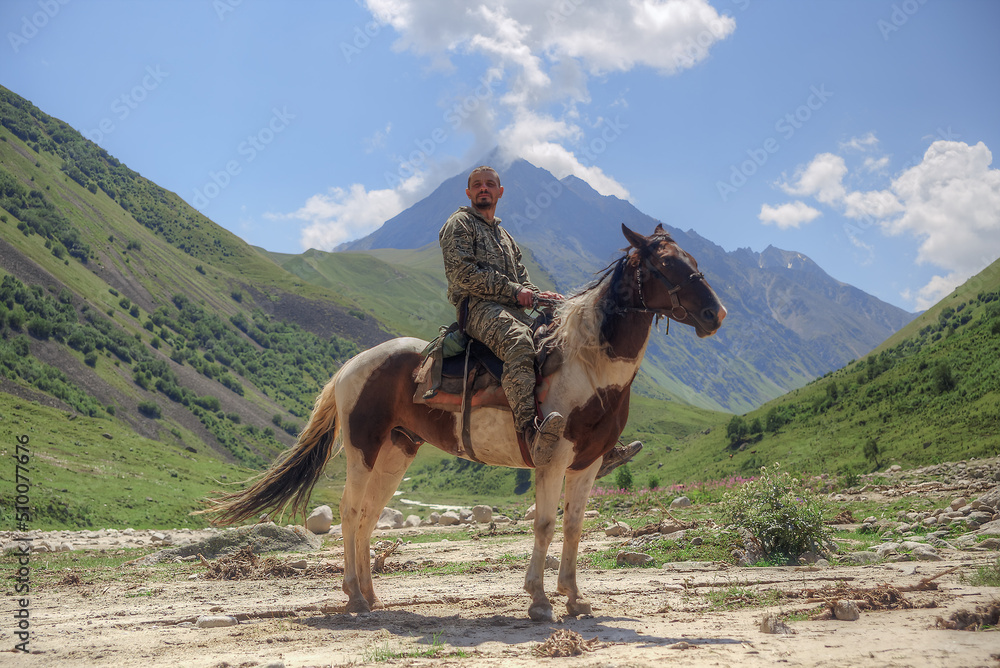Naklejka premium A man is sitting on a horse. In the background is a mountain valley.