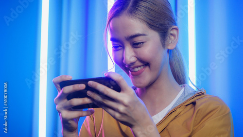 Gamer woman controlling smart phone for video game. Teenage girls leisure game in neon light room at home. photo