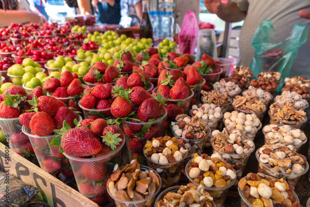 Close-up of strawberries, nuts, dried fruits, cherries, medlar in plastic cups. Counter with fruits, berries and dried fruits, a tourist place.