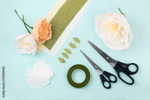 Hand made crepe paper flowers, leaves, scissors and floral tape flat lay.  Paper peony DIY concept photo