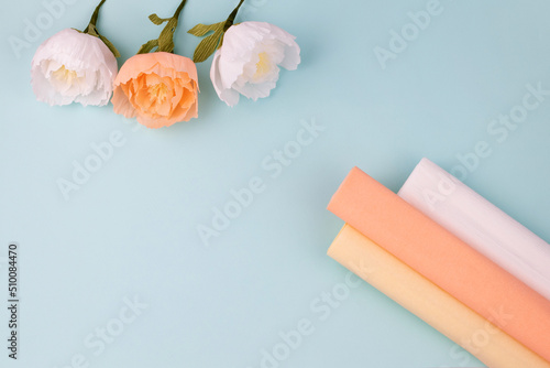 Hand made crepe paper peonies with paper rolls on blue background flat lay. Paper peony DIY concept
