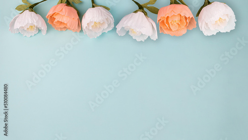Hand made crepe paper peonies on blue background flat lay 16:9. Paper peony DIY concept