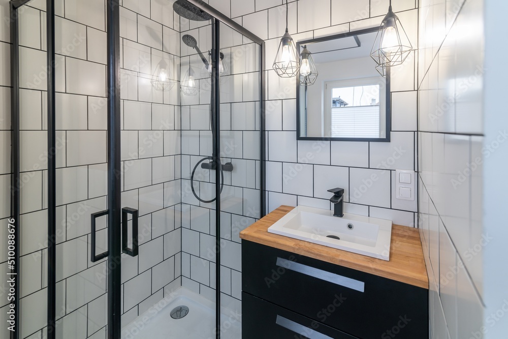 Modern bathroom with a washbasin and a shower cubicle. White tiles on the walls and black joints