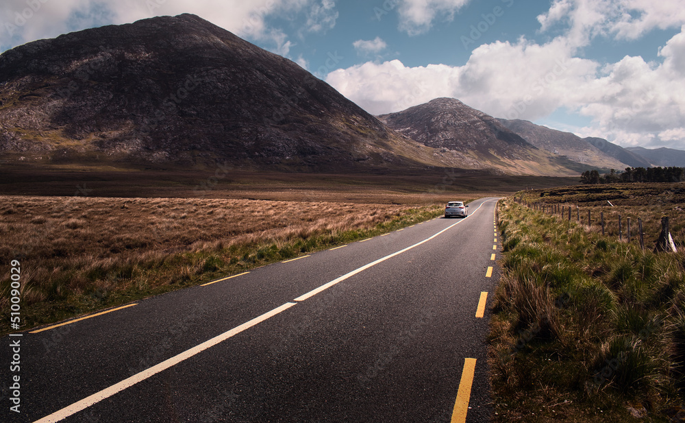 Dramatic landscape scenery with car driving on empty scenic road trough mountains and nature at Connemara National park in county Galway, Ireland