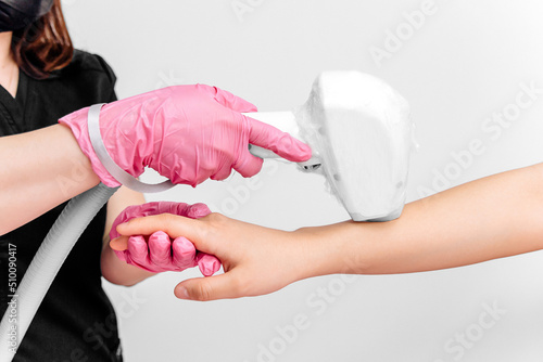 Laser hair removal on the hand on a white background. Pink gloves hold the epilation device on a gray light background, the hands of the doctor remove hair on hands with a laser device photo
