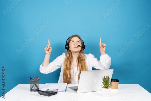 Telemarketing operator pointing above to copy space. Young virtual assistance worker isolated on blue background. photo