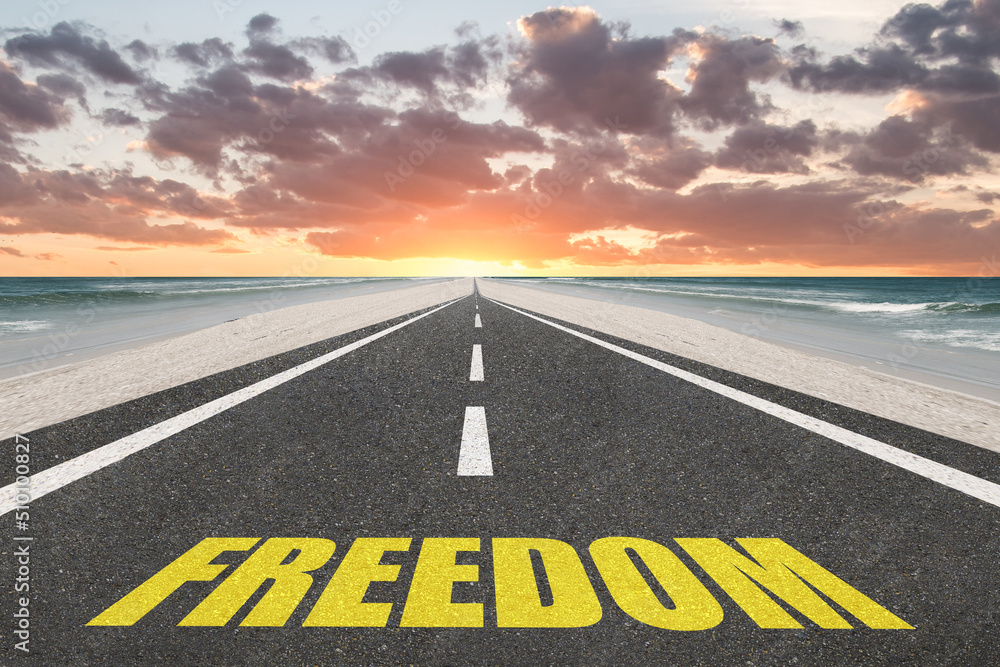 Freedom word on a highway at the beach at sunset for happiness concept.