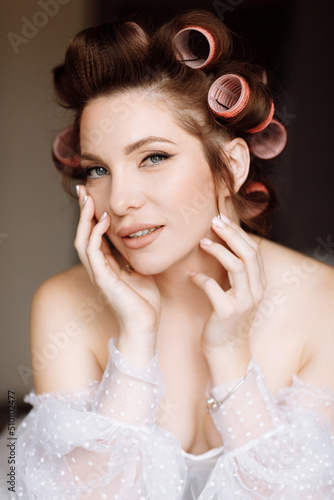 A beautiful young showy brunette woman with bright pin-up make-up in long white lace dress and pink curlers. beauty concept. international women s day.