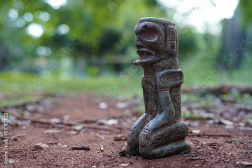 Canvas Print Taino Antique Kneeling meditative Stone Cemi Idol God Figure standing over red dirt on the ground, close up