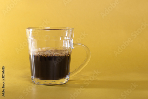 Glass cup with black coffee isolated yellow background
