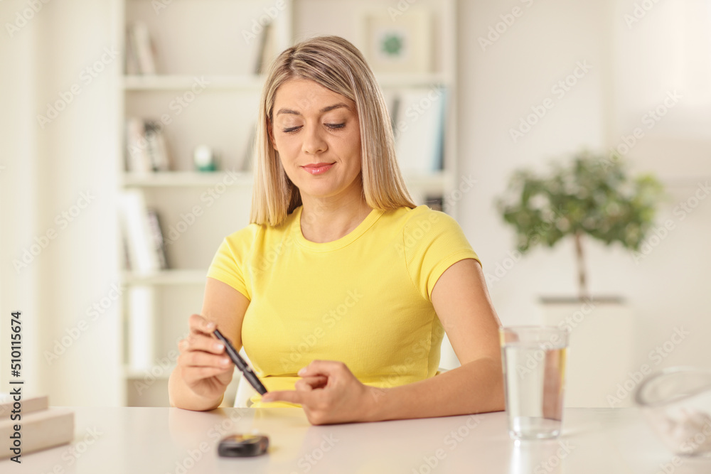 Young woman sitting at home and checking blood sugar level with a pen Young woman sitting at home and checking blood sugar level with a pen