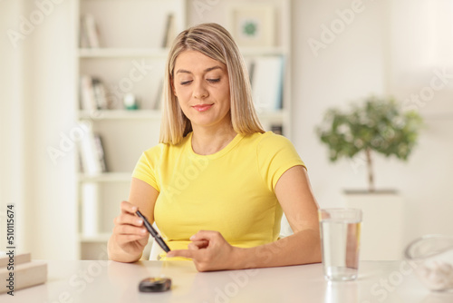 Принти на полотні Young woman sitting at home and checking blood sugar level with a pen