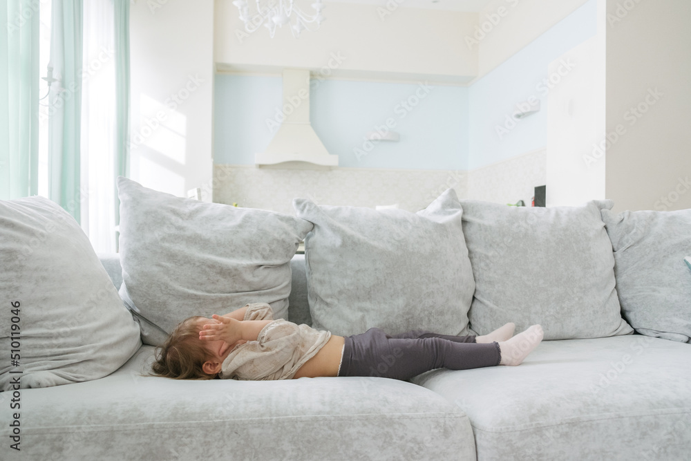 little girl lies on a large bright sofa in a spacious apartment little girl lies on a large bright sofa in a spacious apartment
