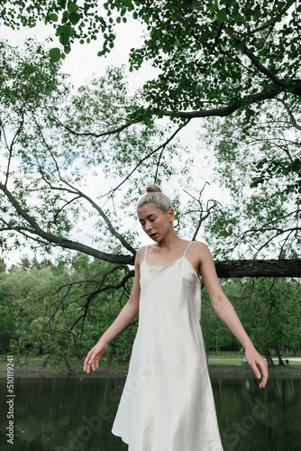 girl in a white flying dress on a walk in the woods against the background of the lake photo