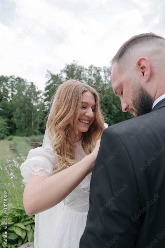 portrait of a young laughing bride as she hangs a boutonniere to the groom in front of the garden portrait of a young laughing bride as she hangs a boutonniere to the groom in front of the garden