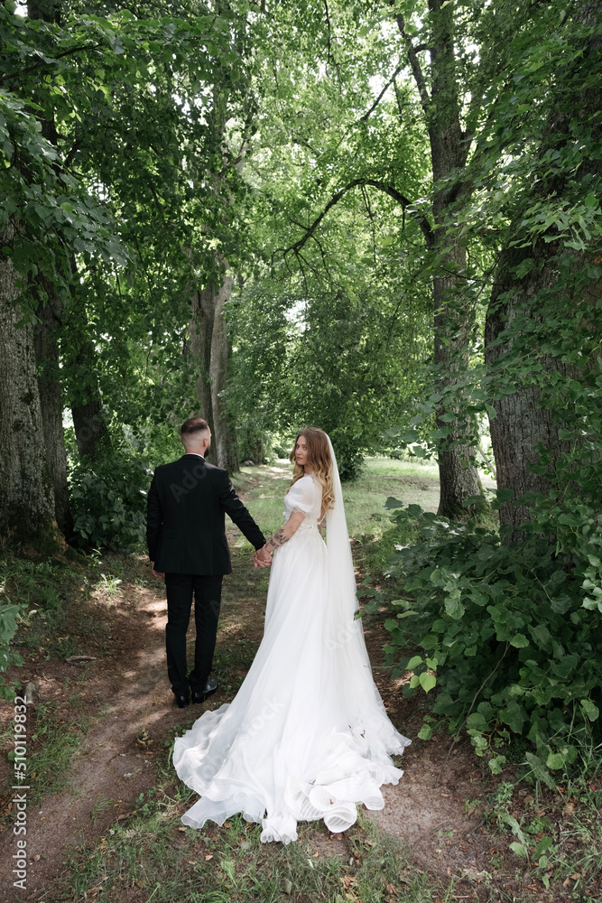 the bride and groom are walking in the woods, a long train of the bride's dress is spread on the ground the bride and groom are walking in the woods, a long train of the bride's dress is spread on the ground
