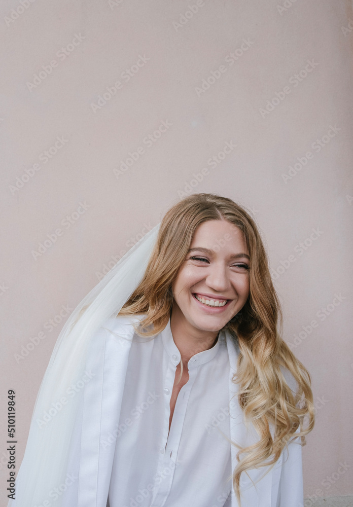 portrait of a laughing bride in a veil and white shirt on a light background portrait of a laughing bride in a veil and white shirt on a light background