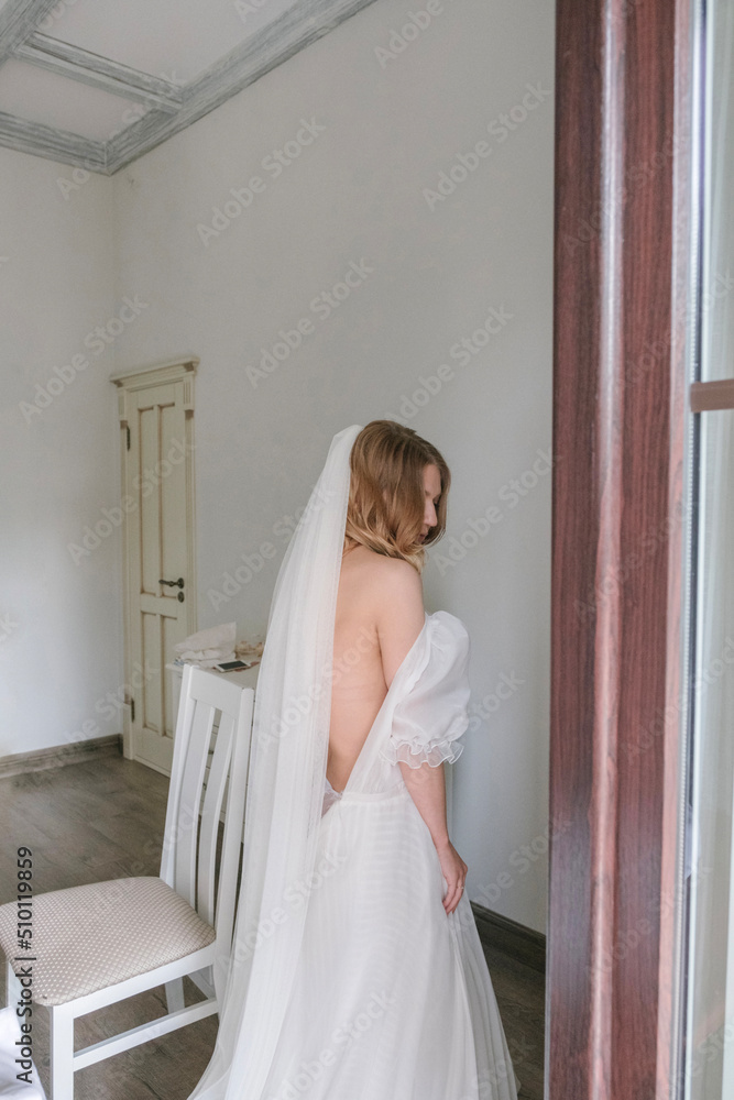 photo of the bride with a veil, who wears a dress in a bright room before the wedding photo of the bride with a veil, who wears a dress in a bright room before the wedding