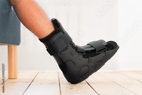 Injury man with black splint on leg sitting on the sofa at home. Ankle foot orthosis close-up. © mallmo