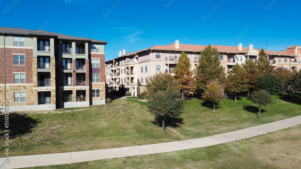 Aerial view multistory apartment building with concrete pathway sidewalk and colorful fall foliage in sunny autumn day near Dallas, Texas, America