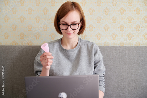 A teenager with a menstrual cup in his hands sits with a laptop photo