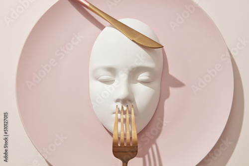 Plaster white mask served on pink plate with golden cultery