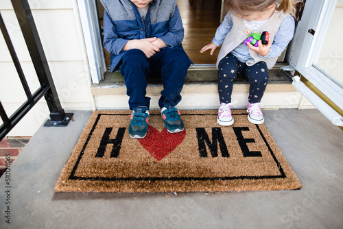 Children sitting on front porch of home with welcome mat photo