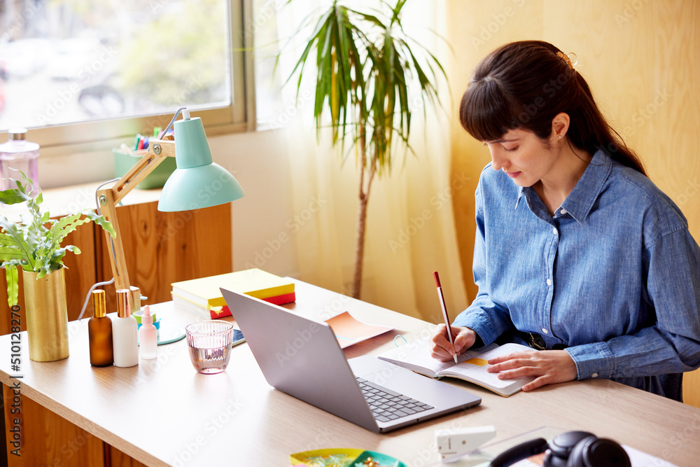 Woman taking notes while working on laptop Woman taking notes while working on laptop