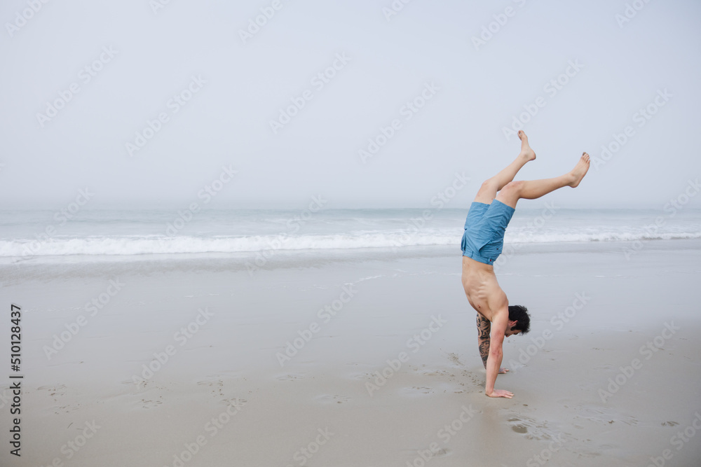 Man doing hand stand on sand.