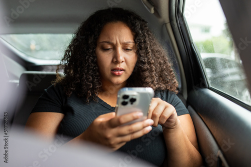 Woman Looks Concerned While Using Smart Phone In Backseat Of Car