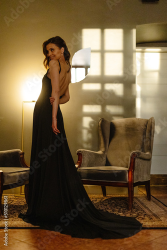 Elegant Woman In Long Black Dress Posing In Sunny Apartment photo