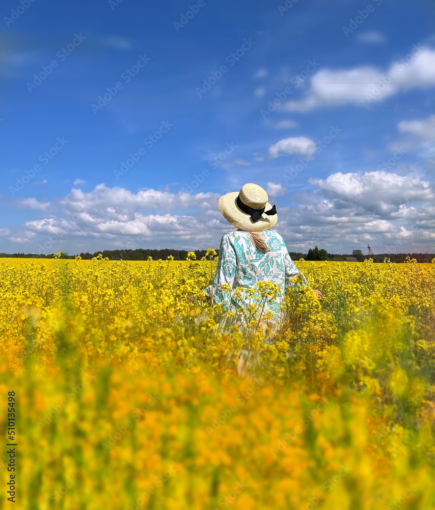 woman in wrap hat and blue dress on wild field blossom yellow flowers and bright sky with white clouds summer nature landscape