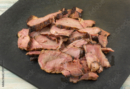 Slices of cooked beef brisket on black cutting board on table