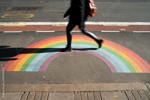 A woman walks over a Rainbow sign on a street photo