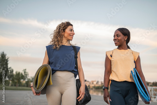 Caucasian woman and black woman in sportswear walking along a river in